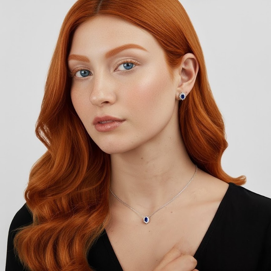 Set di gioielli con zirconi blu e bianchi, indossato da una donna dai capelli rossi su sfondo bianco. La collana presenta un ciondolo ovale con zircone blu centrale e contorno di zirconi bianchi, abbinato a orecchini a lobo dello stesso design.