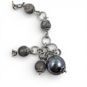 Bracciale artigianale in argento con sfere di pietra di luna grigia, maglie circolari intrecciate e una grande perla grigio scuro pendente su fondo bianco.