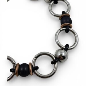Bracciale artigianale composto da anelli in acciaio lucido alternati a sfere nere e lucide con chiusura a moschettone brunita su fondo bianco.
